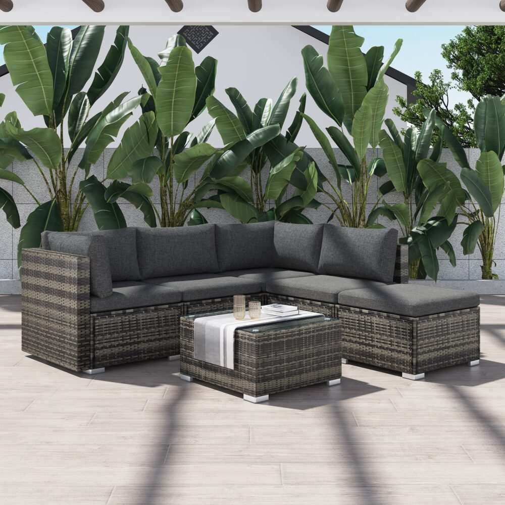 Ottoman-Style Outdoor Lounge Set in Grey with PE rattan wicker and glass-top table, arranged in an L-shape, on a patio with greenery backdrop.