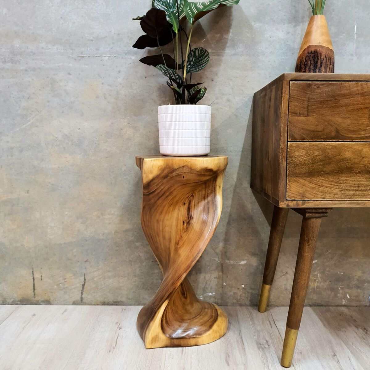 Heart-shaped twisted stool made from hand-carved Raintree wood, used as a side table or bar stool, with a plant on top.